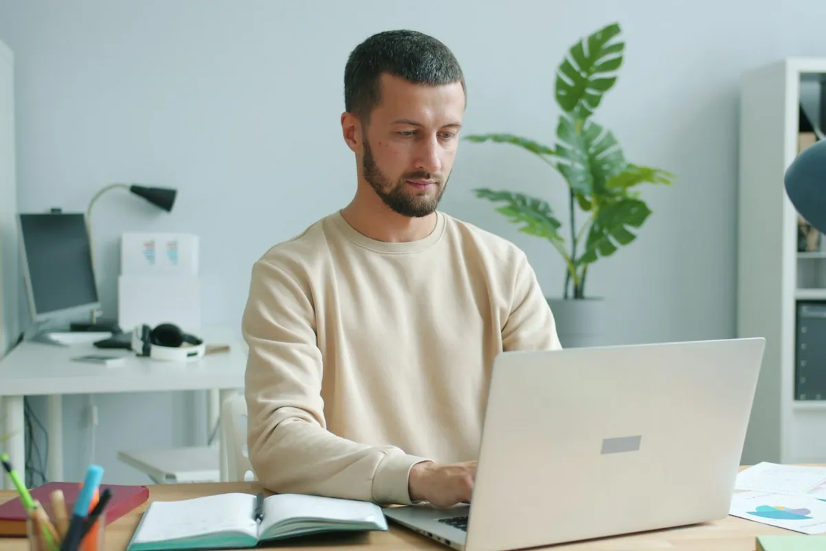 A man working on a laptop with notes in a home office